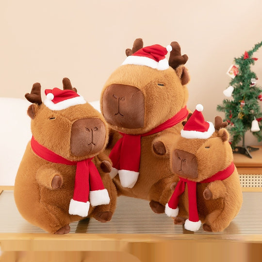 Three festive capybaras sitting on a table. Christmas Plushie, Capybara Plushie, Squishmallow.